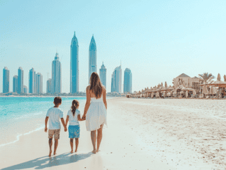 Dubai mit Kindern. EIne Mutter geht mit ihren Kindern über den weissen Sandstrand. Im Hintergrund ist die Skyline von Dubai zu sehen. rechts ist ein Beach Club